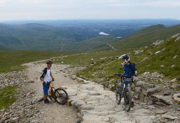 Two cyclists dismount to push their bikes up cobblestone on Llanberis Path.
