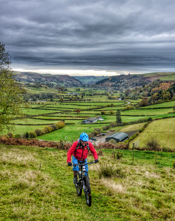 Cycling the Trans Cambrian Way with patchwork green fields in the background