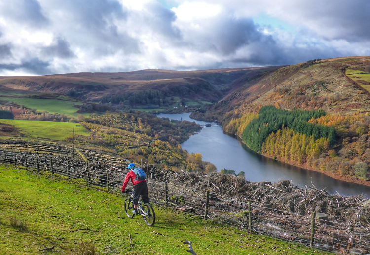A cyclist rides along the Trans Cambrian Way with the Claerwen Reservoir below